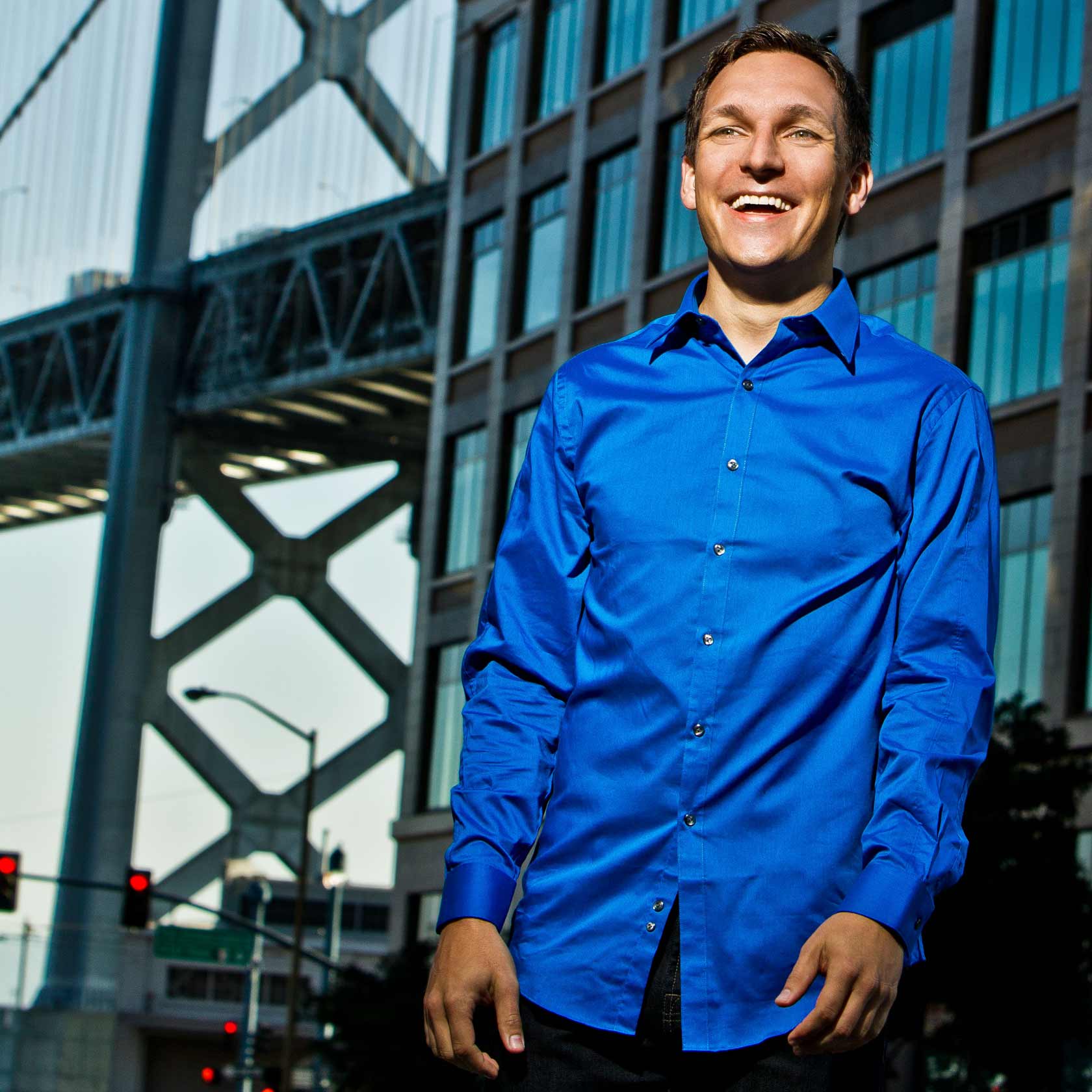 Gabor Cselle in a blue shirt, smiling, in front of the Bay Bridge